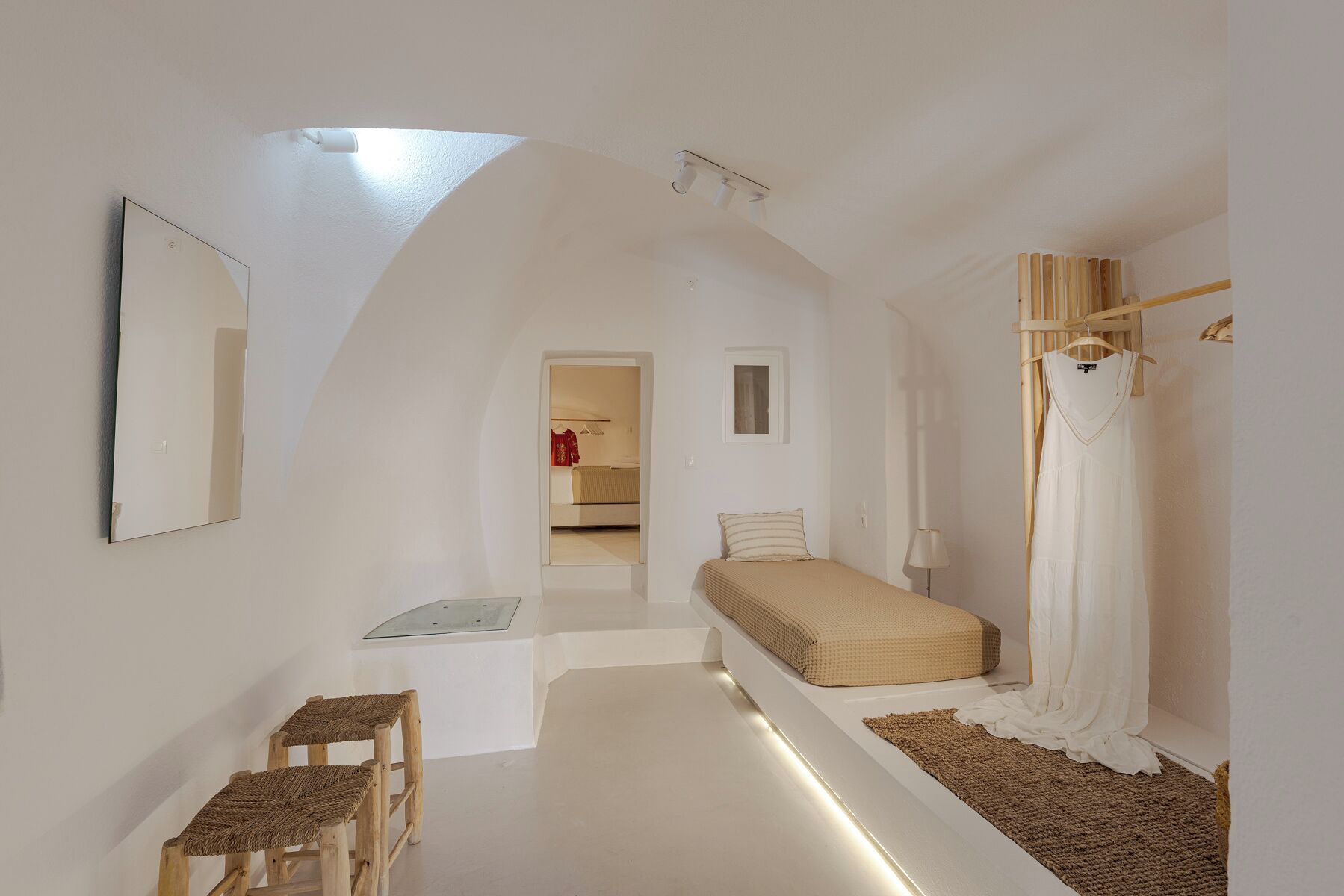 A narrow room with a sloped ceiling, a bed, a small table, a chair, and a mirror.