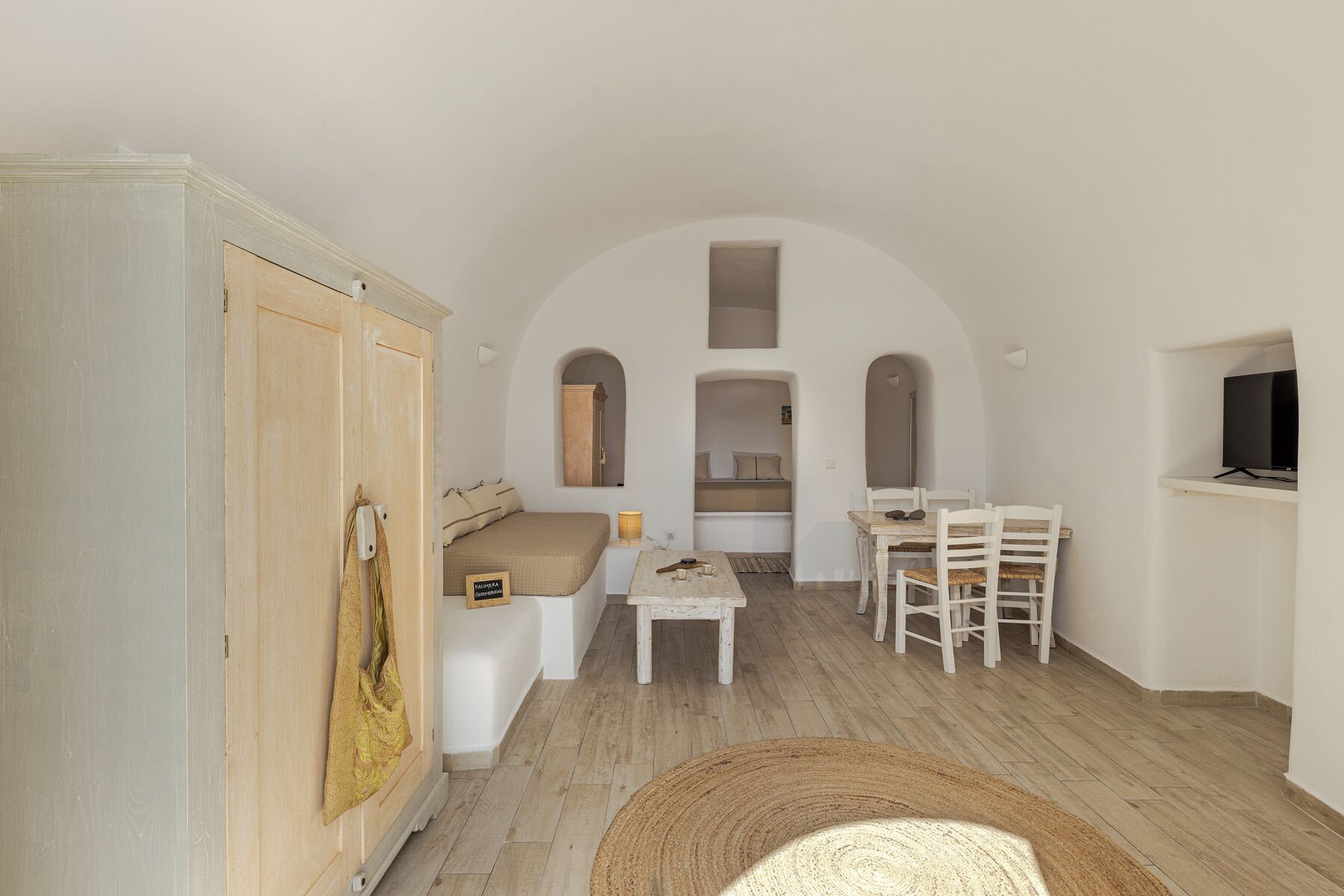 Quarto compacto com cama, uma mesinha e televisão.