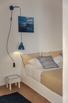A bedroom with a bed, a nightstand, a lamp, a wall-mounted picture, and a small table.