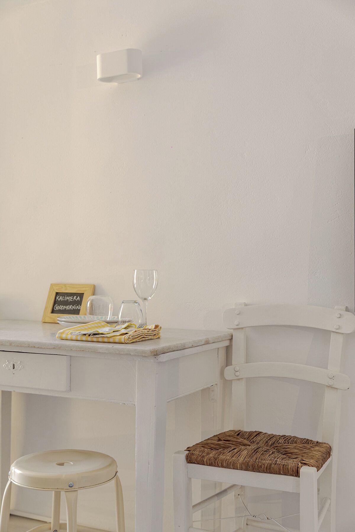 A white wooden desk with a chalkboard sign, two wine glasses, a folded cloth, and a wicker chair.