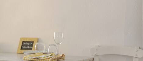 Un escritorio de madera blanca con un cartel de pizarra, dos copas de vino, un paño doblado y una silla de mimbre.