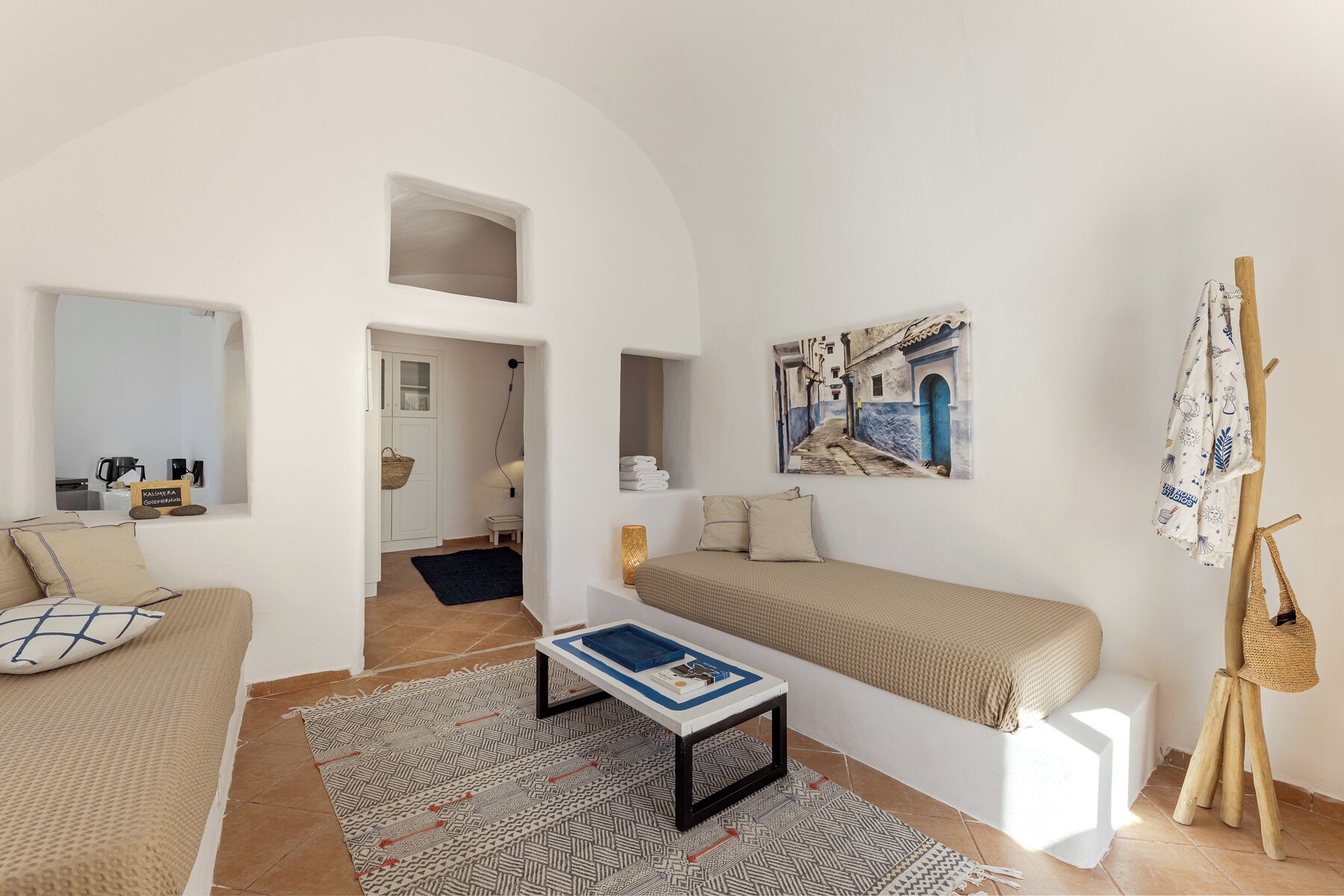 Una habitación minimalista con una cama, una mesita, un cuadro y un caballete de madera.