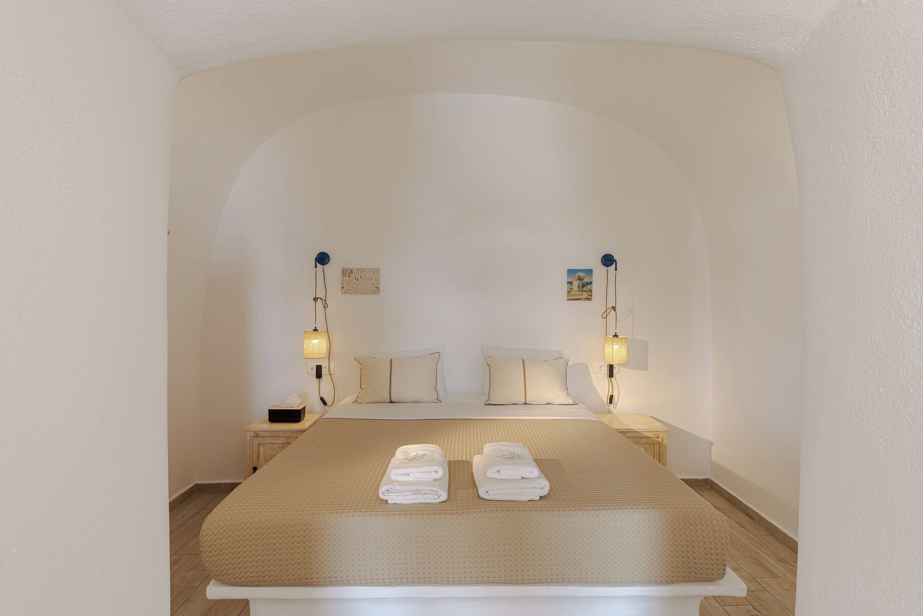 Un dormitorio con una cama, dos mesitas de noche, dos lámparas de pared y un perchero con toallas.