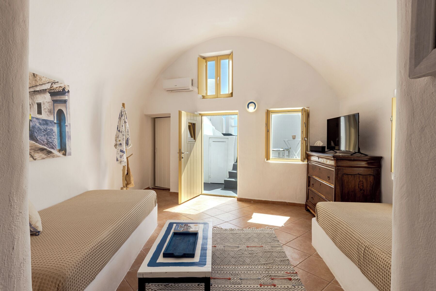 A compact living space with a bed, a TV, a small table, and a door leading to a staircase.