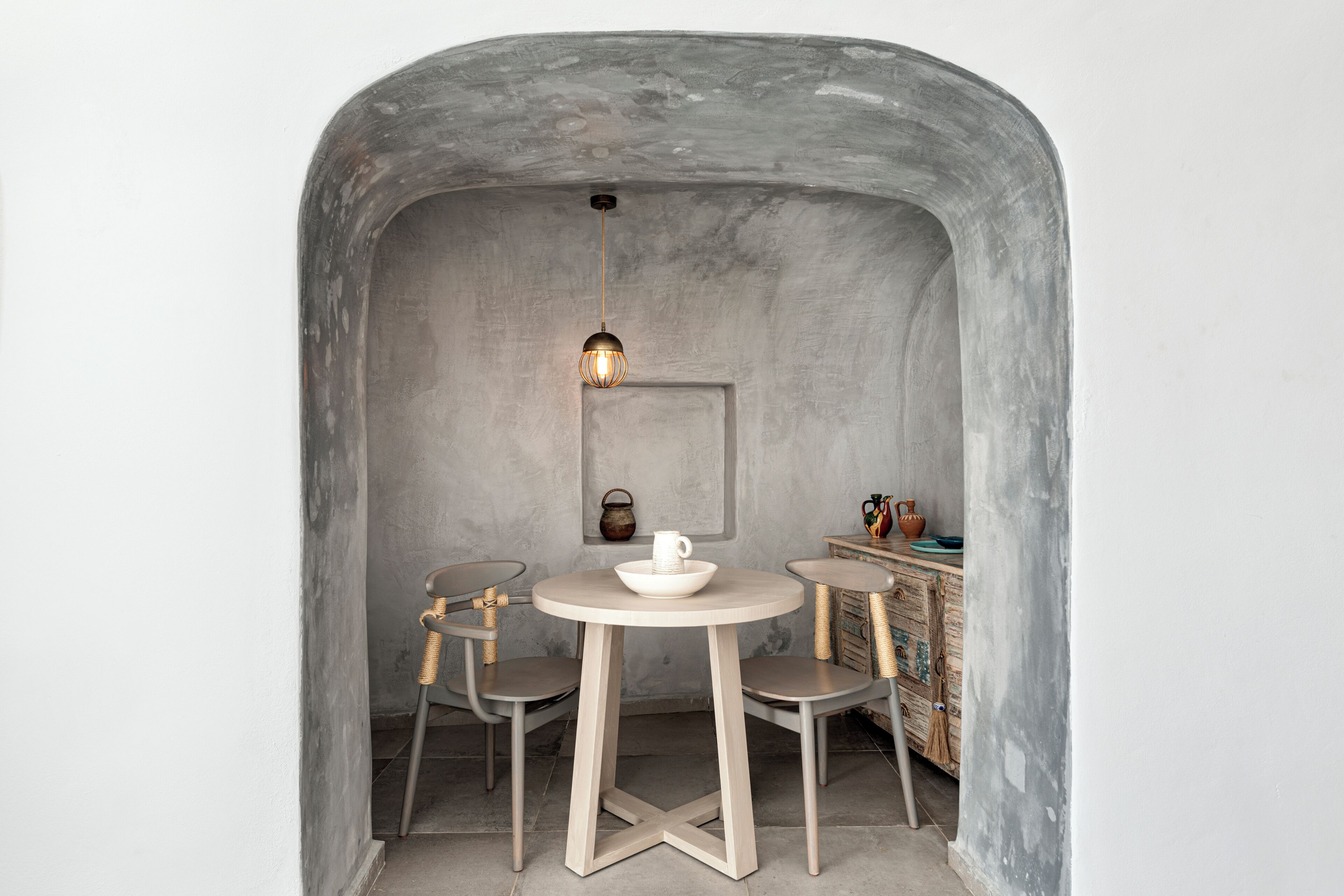 A small, cozy dining area with a round table and two chairs, a hanging light fixture, and rustic decor.