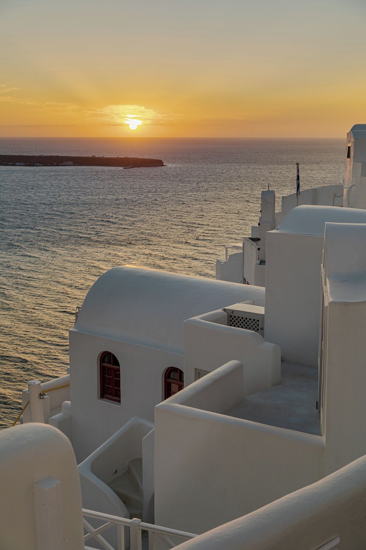 A coastal building with white walls and red doors, overlooking the sea at sunset.
