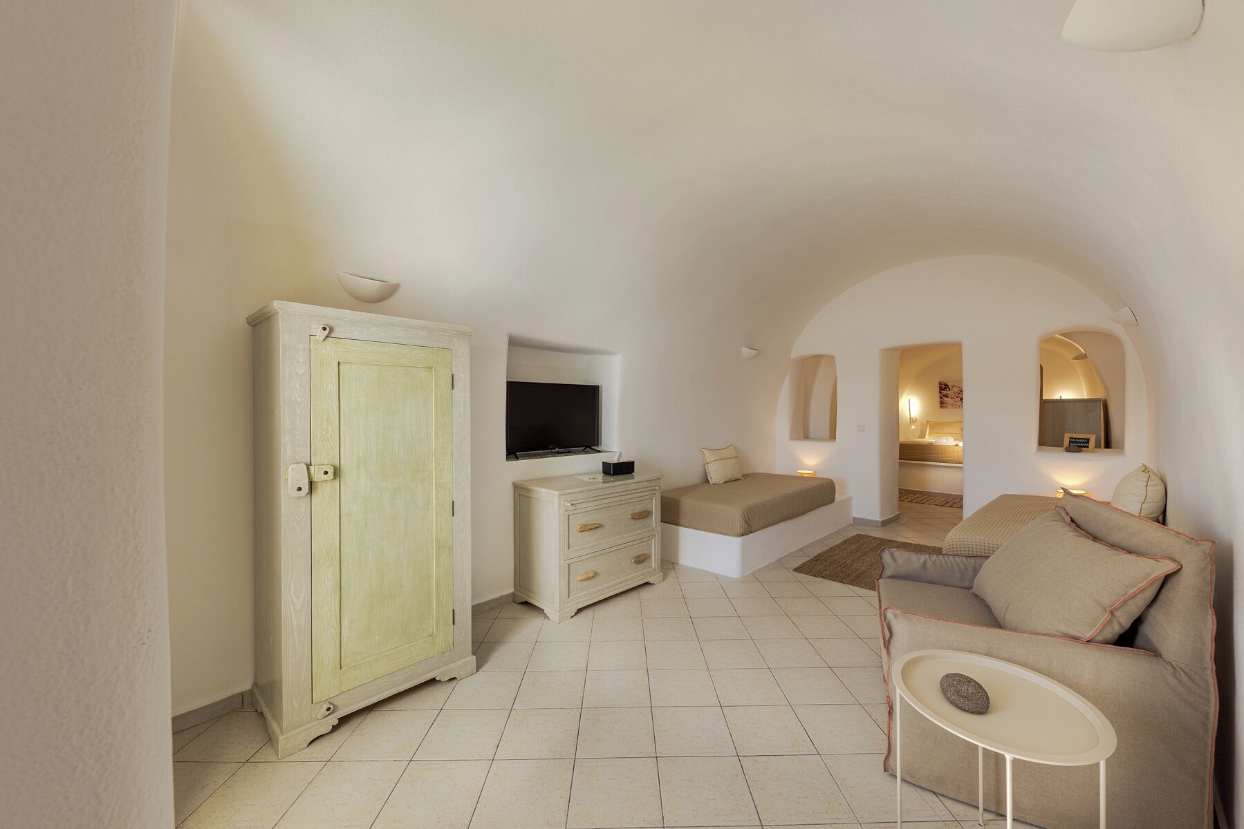 A spacious room with a large wardrobe, a television, a sofa, and a small table.