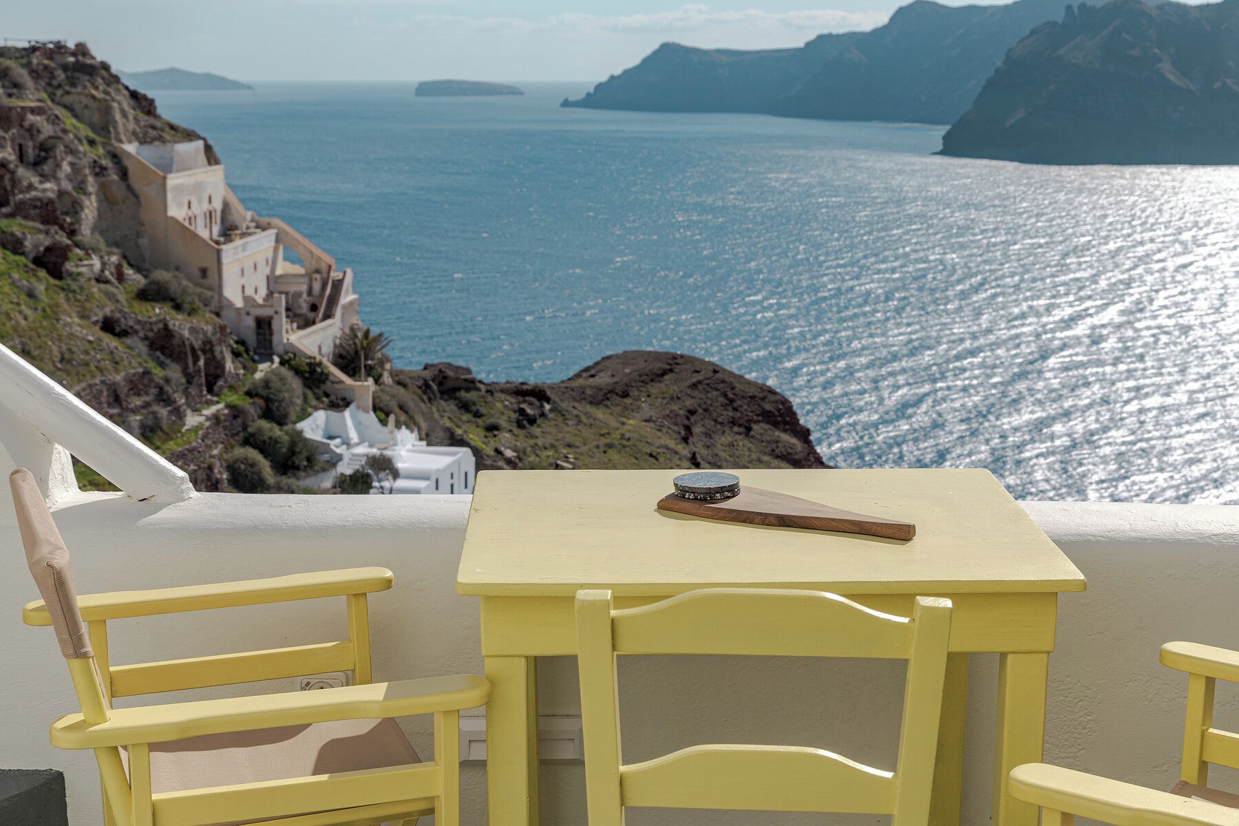 A yellow table and chair set with a view of the sea and coastal buildings.