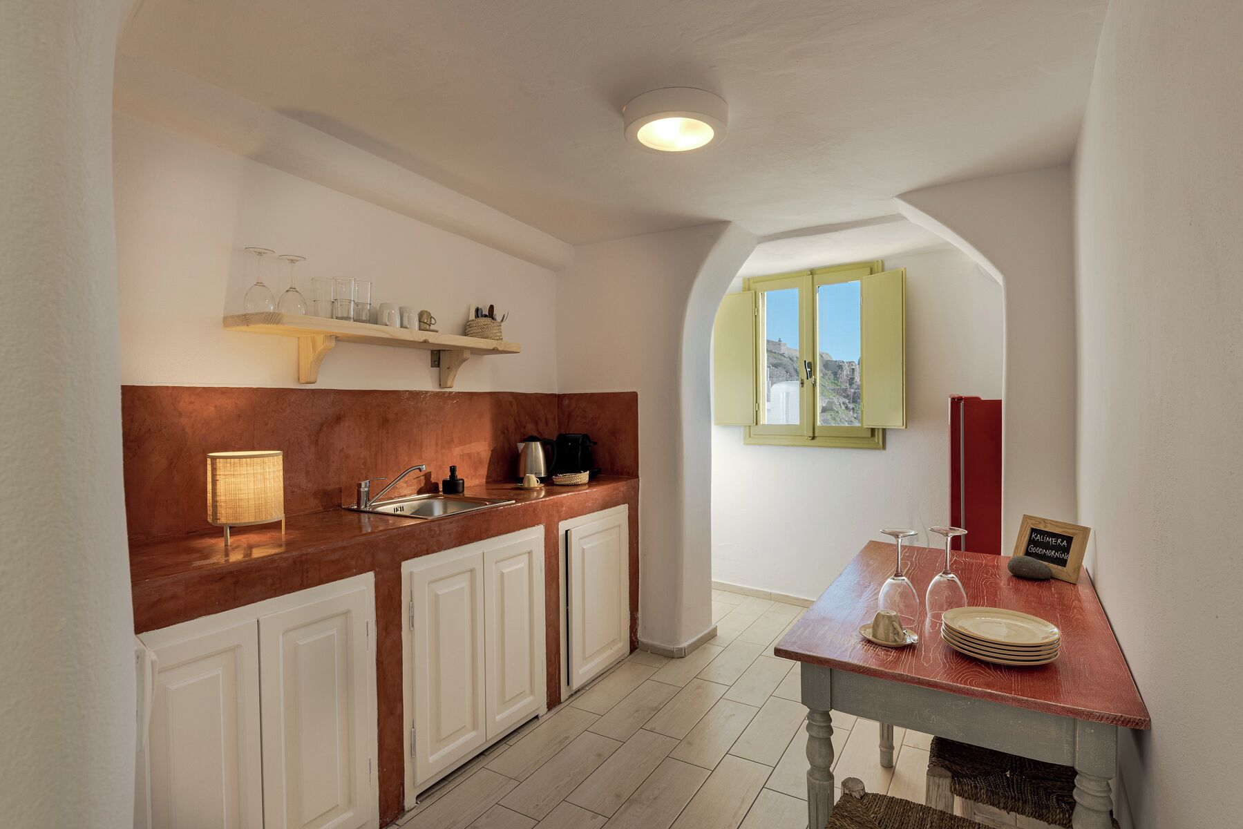 A kitchen with a wooden countertop, white cabinets, a hanging shelf, and a window with a view.
