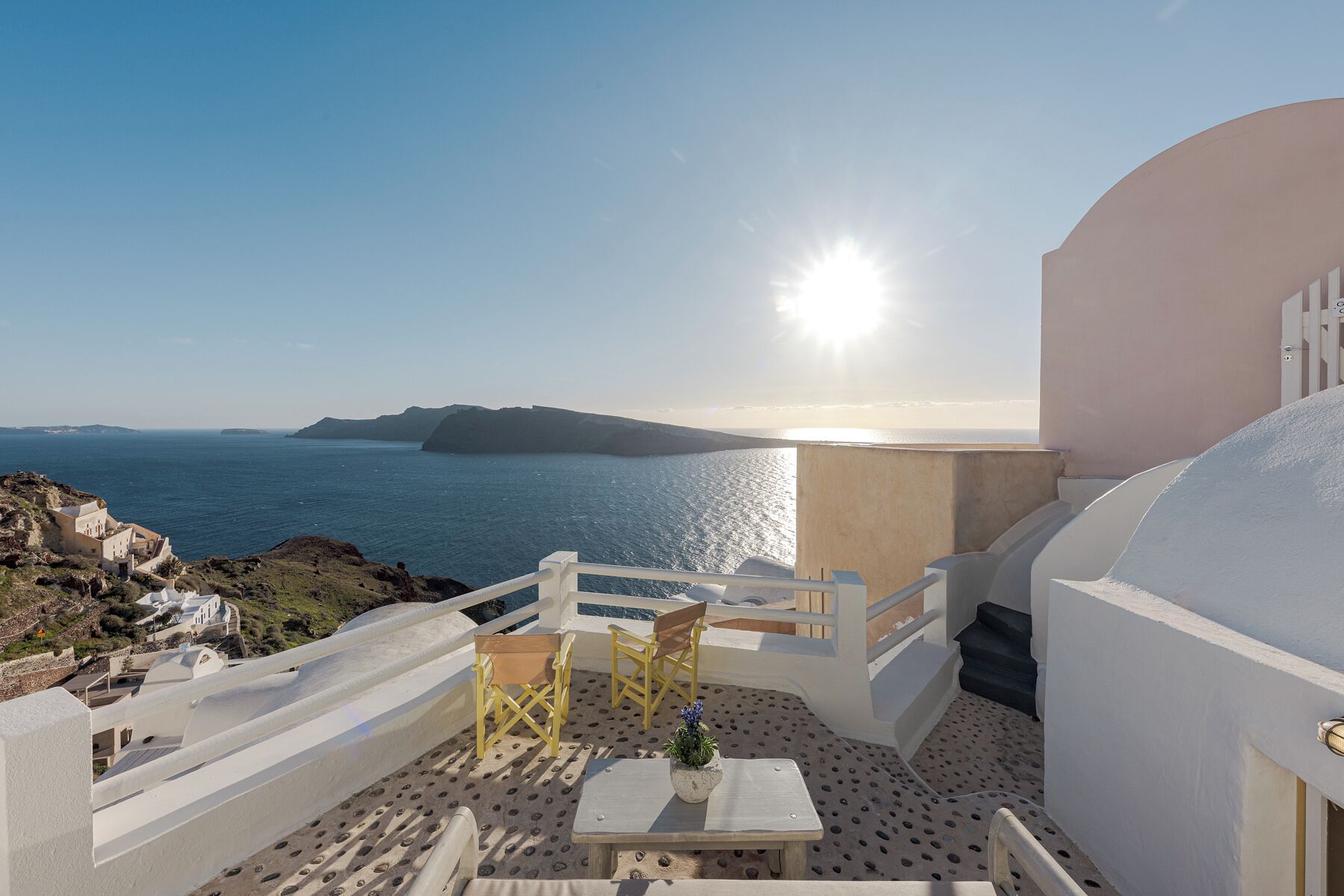 A terrace with a table, chairs, and a potted plant overlooking the sea.
