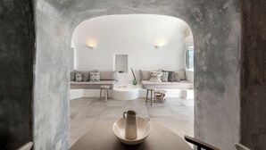 A modern interior with a stone archway, a central seating area with sofas and a coffee table, and a vase on a table. - Just Blue (Santorini)