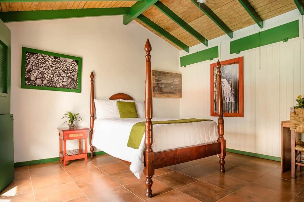 A four-poster bed with a wooden frame, a green throw blanket, and a small bedside table with a plant.