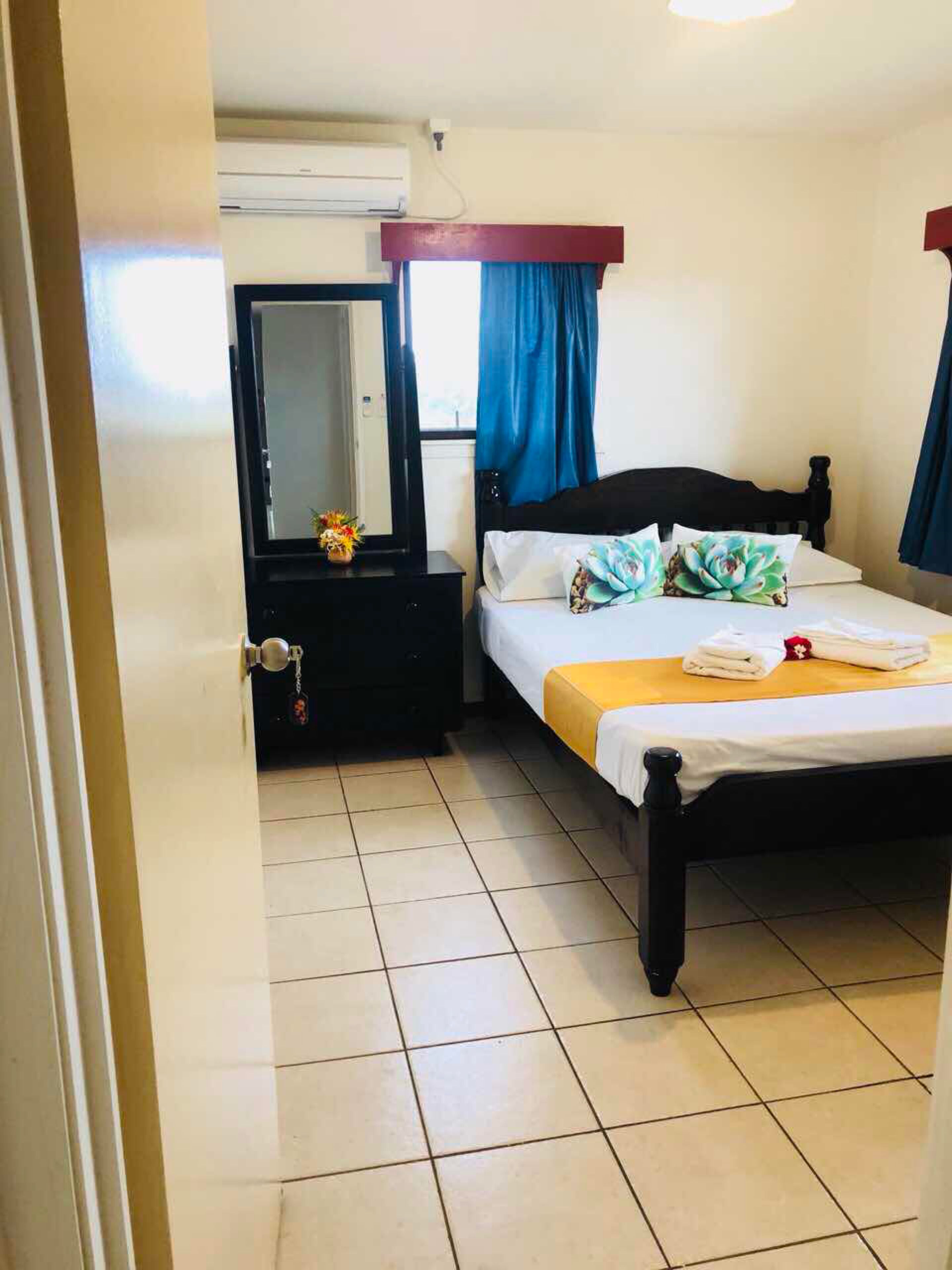 Una habitación de hotel con cama, mesita de noche, espejo y ventana con cortinas.