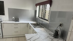 Una cocina con armarios blancos, encimera de mármol, un fregadero, una ventana con reja de metal y un hervidor.