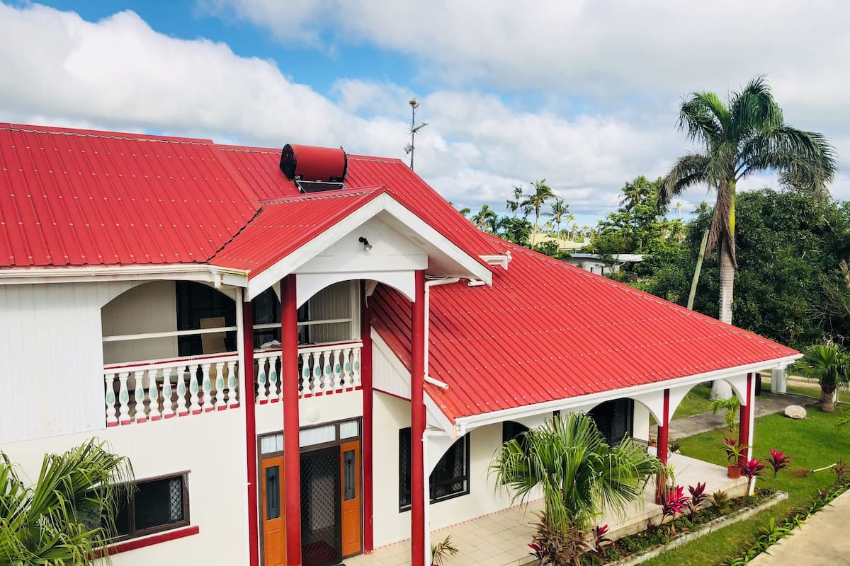 A two-story building with a red roof, white walls, and a balcony with a red railing.