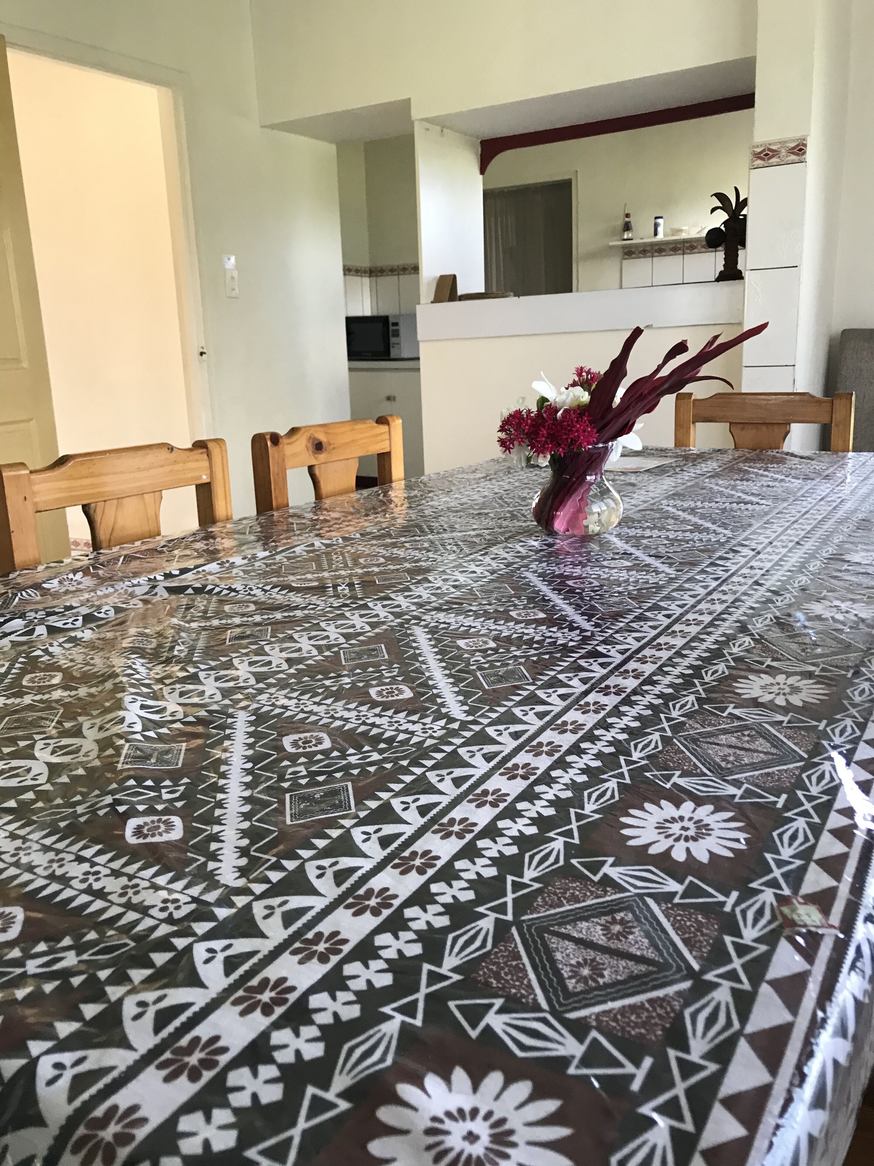 A dining table with a patterned tablecloth, wooden chairs, and a vase with flowers.