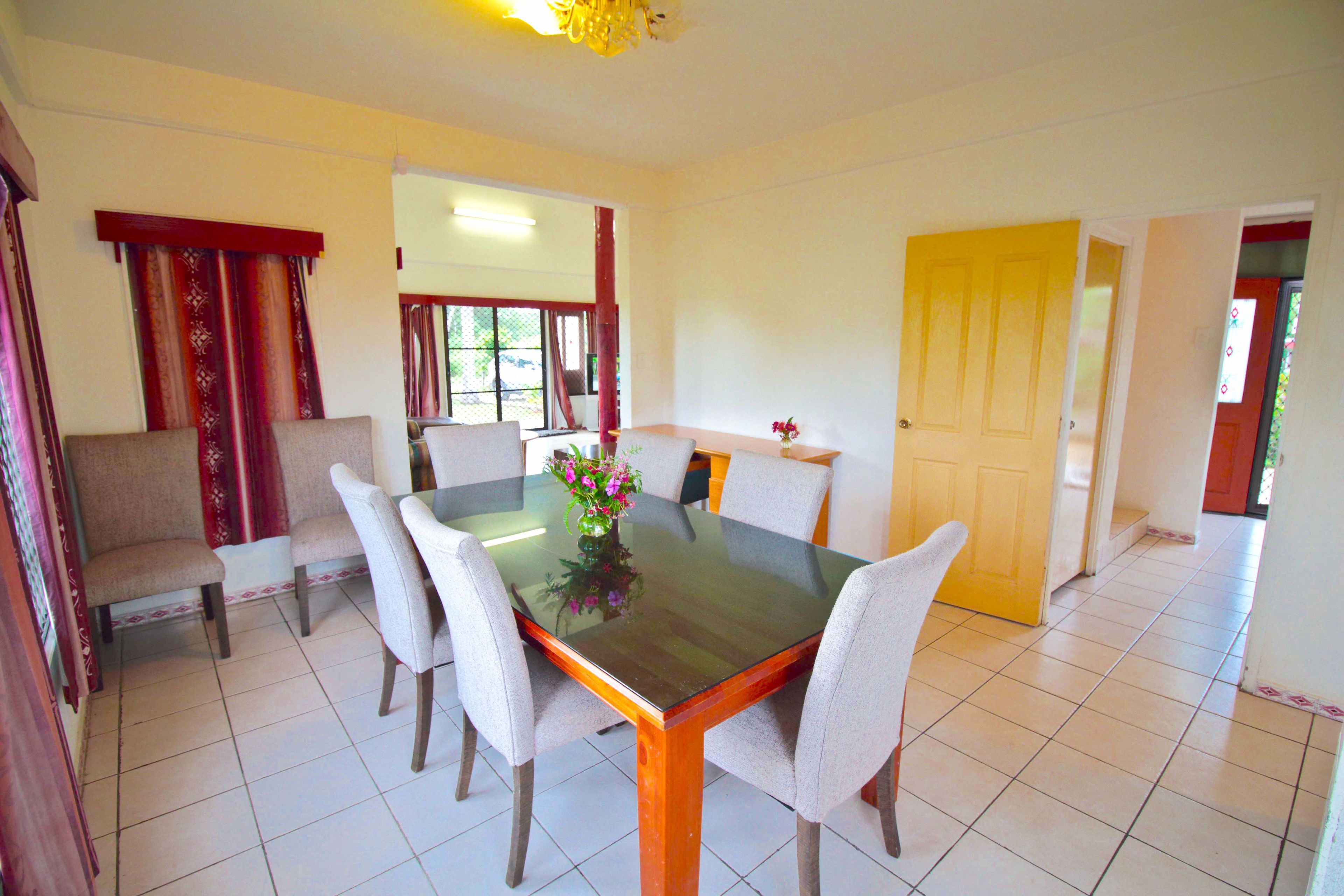 Un coin repas comprenant une table avec un plateau en verre, six chaises et un vase rempli de fleurs.