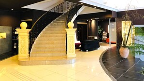 A modern hotel lobby with a central staircase, a reception desk, and a large potted plant.