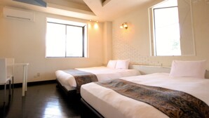 A hotel room with two beds, a desk, and large windows.