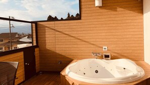 A modern bathroom with a wooden floor, a large freestanding bathtub, and a window overlooking a residential area.
