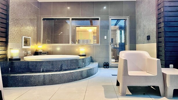 A modern bathroom with a large bathtub, a separate shower area, and a seating area with a chair and table.