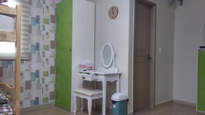 Una habitación con una cama, un escritorio con espejo, un cesto de basura y una puerta.