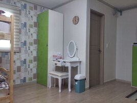 Una habitación con una cama, un escritorio con espejo, un cesto de basura y una puerta.