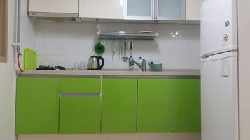 A kitchen with green cabinets, a white countertop, a kettle, and a refrigerator.