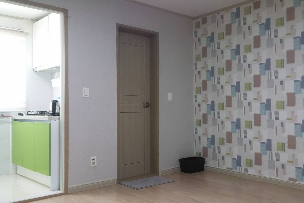 Quarto com porta para cozinha, parede estampada e uma pequena lixeira preta.