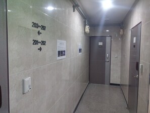 Un pasillo con señales indicativas para las habitaciones 203 a 207 y 201 a 202, una puerta con el número 202, y un panel informativo fijado a la pared.