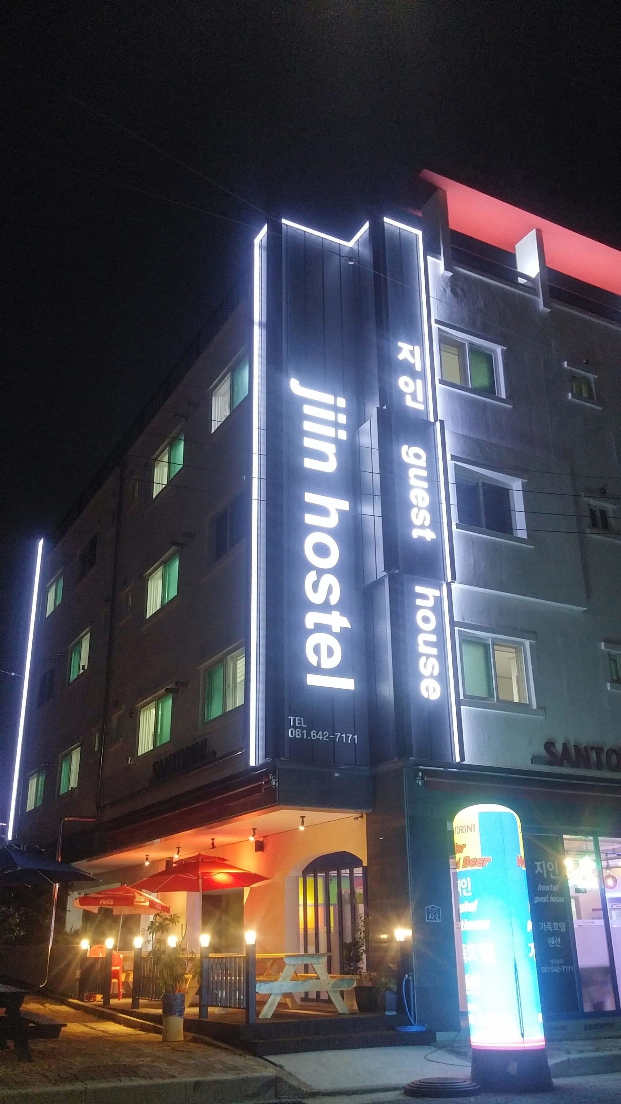 A building with a sign for 'jin hostel' and 'guest house' with a contact number.