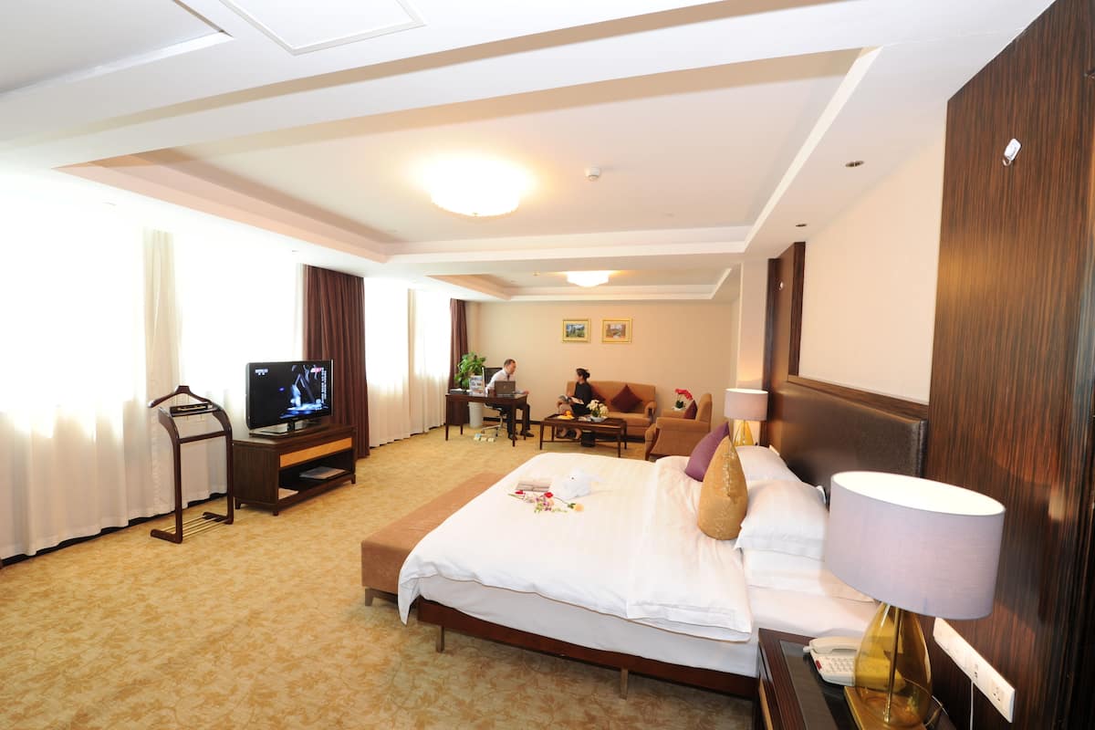 Ein Hotelzimmer mit Bett, Fernseher, Schreibtisch, Stuhl, Sofa und Lampe.