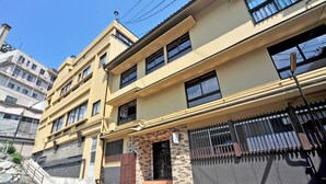 Un edificio residencial de varios pisos con fachada amarilla, numerosas ventanas y entrada con reja.