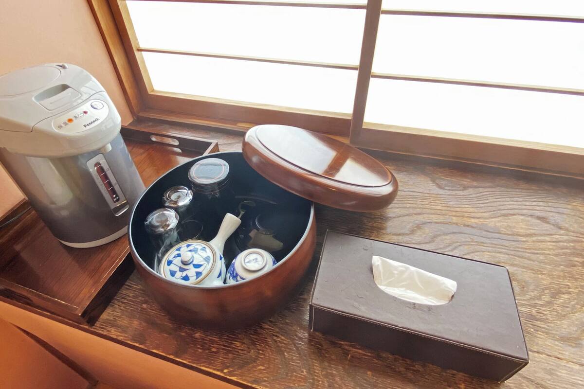 Eine Kaffeemaschine, ein Teekessel und eine Taschentuchbox auf einem Holztablett neben einem Fenster.