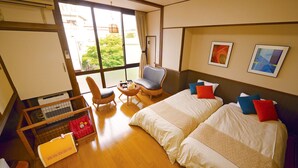 Una habitación de hotel con dos camas, una silla, una mesita pequeña y un ventanal grande.