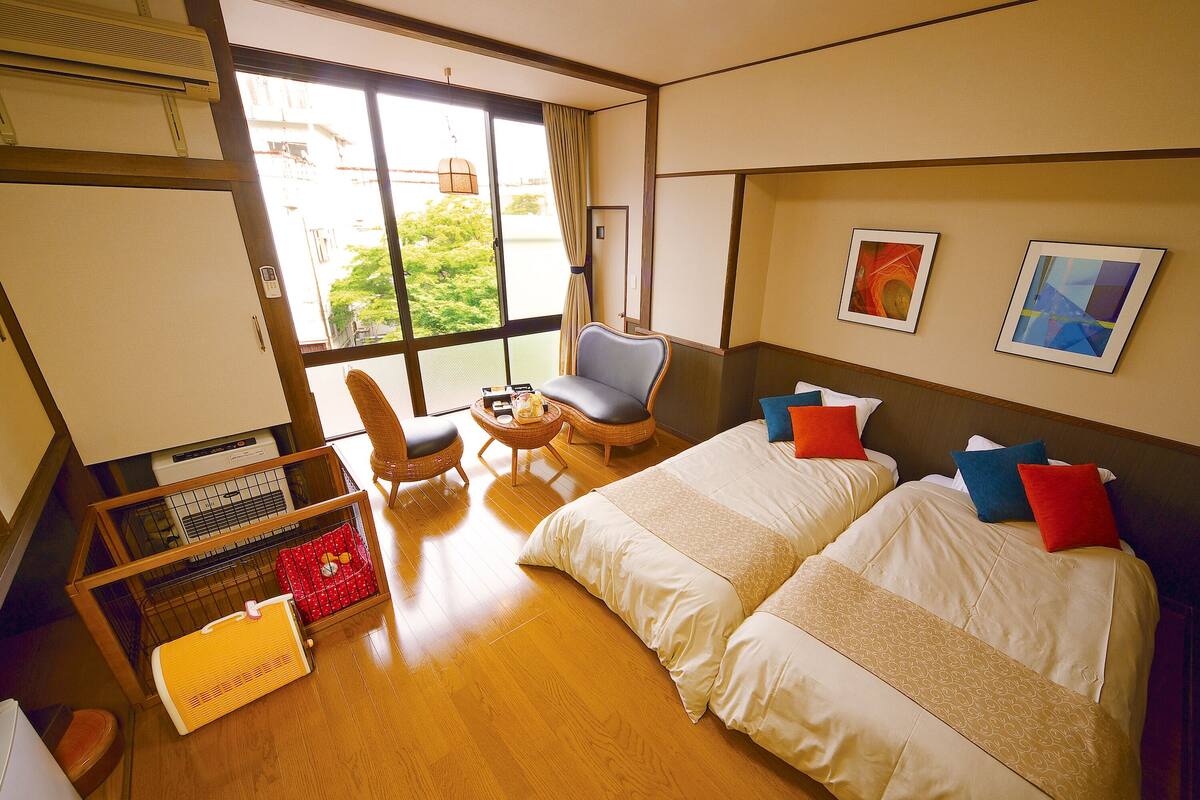 A hotel room with two beds, a chair, a small table, and a large window.