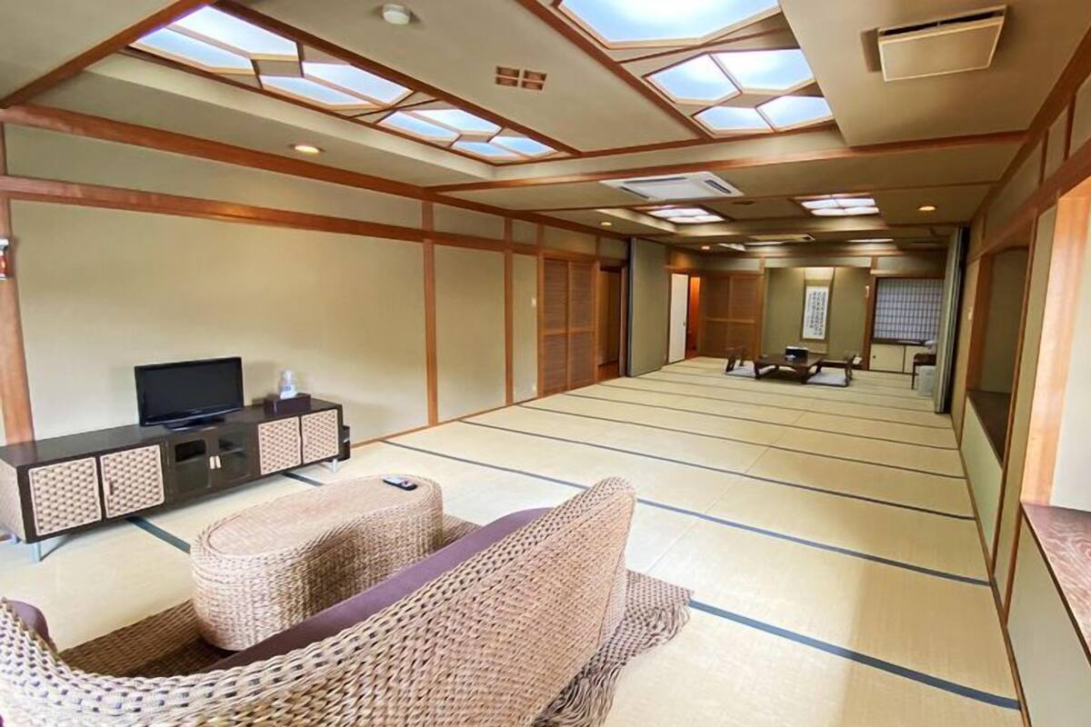 A traditional Japanese-style room with tatami flooring, a low wooden table, a television on a cabinet, and a sliding door leading to another room.