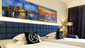 Ein Hotelzimmer mit zwei Betten, einem blauen Kopfteil, weißer Bettwäsche und zwei Stadtansichten an der Wand.