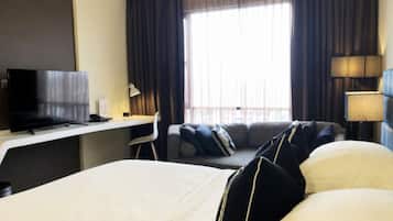 Hotelkamer met een bed, een bureau met een televisie, een stoel, een bank en een raam met gordijnen.