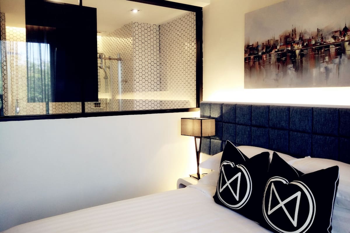 Een hotelkamer met een groot bed, een hoofdbord, een nachtkastje, een lamp, een spiegel en een stadsgezichtschilderij aan de muur.