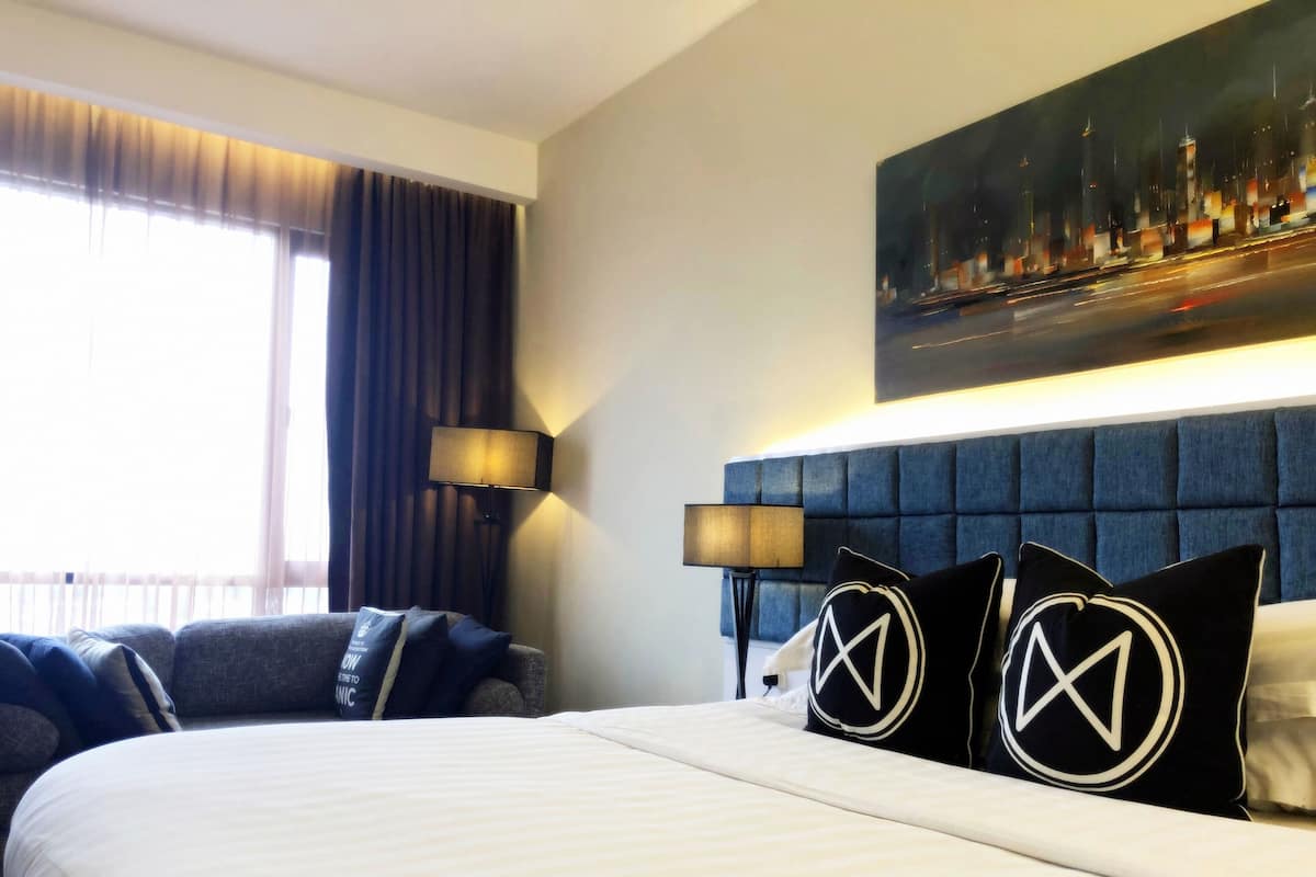Een hotelkamer met een groot bed, een hoofdbord, een stadsgezicht op een schilderij en een raam met gordijnen.