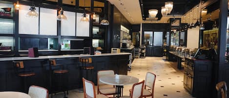 L’intérieur d’un restaurant, avec un bar, des tables rondes et des tabourets de bar.