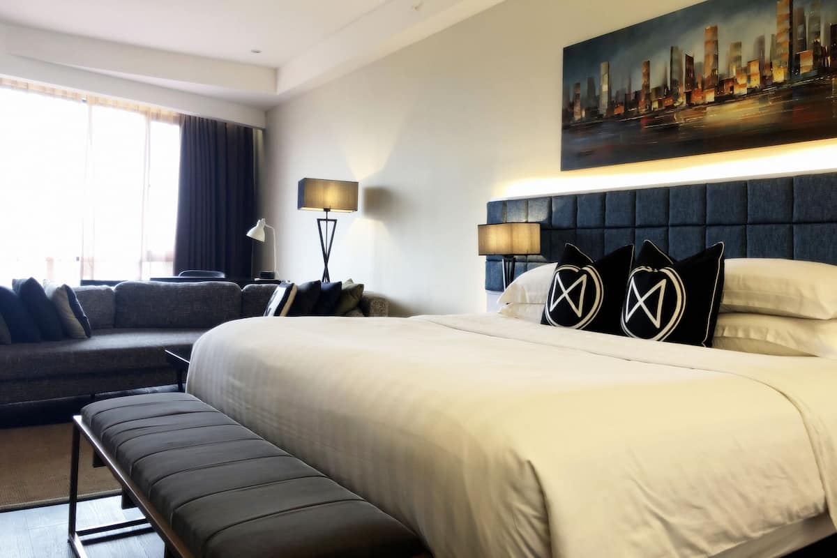 Een hotelkamer met een groot bed, een bank, een houten zitbankje, een schilderij van een stadsgezicht en twee lampen.