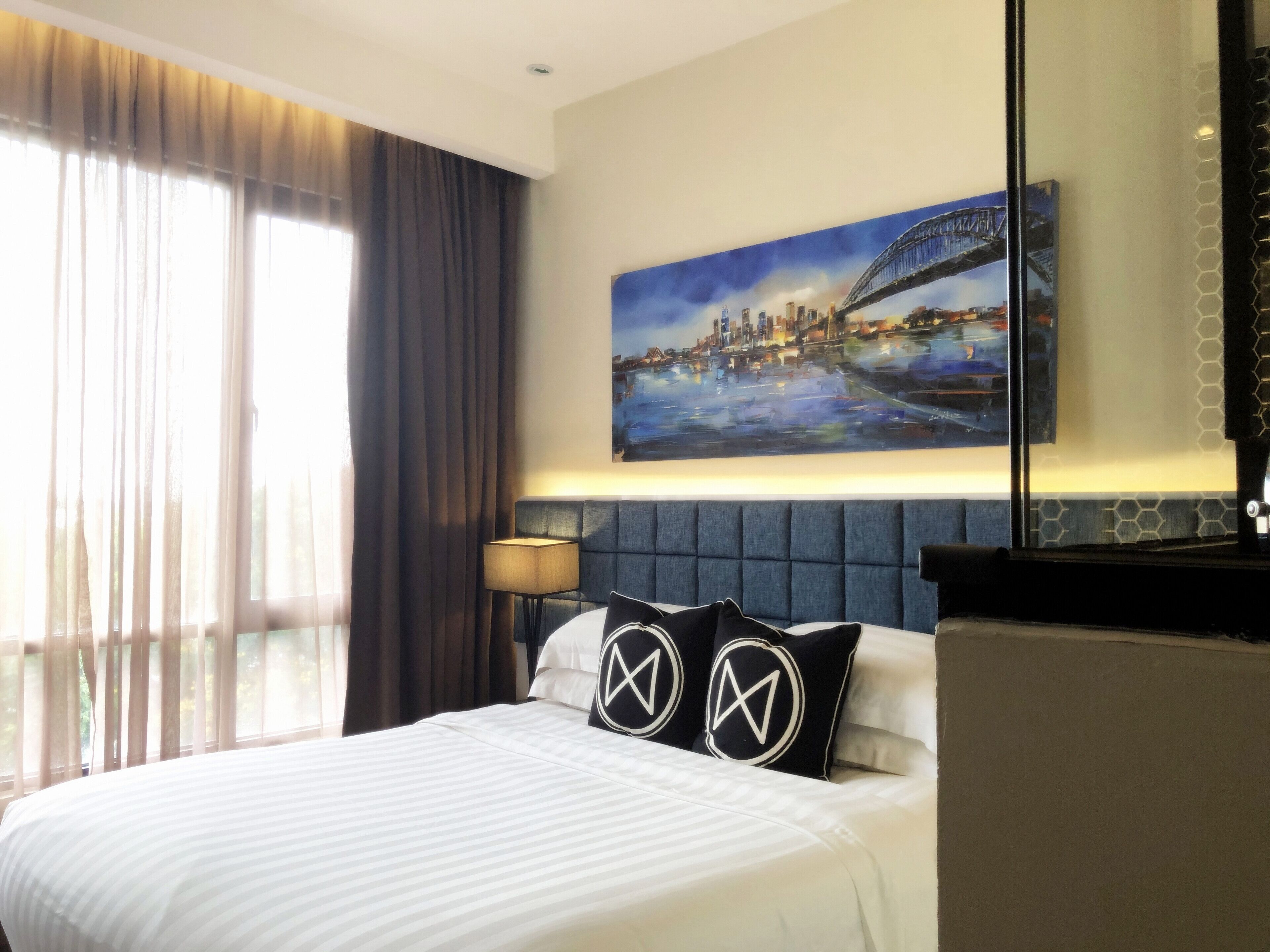 A hotel room with a bed, a painting of a bridge, and a view of the city.