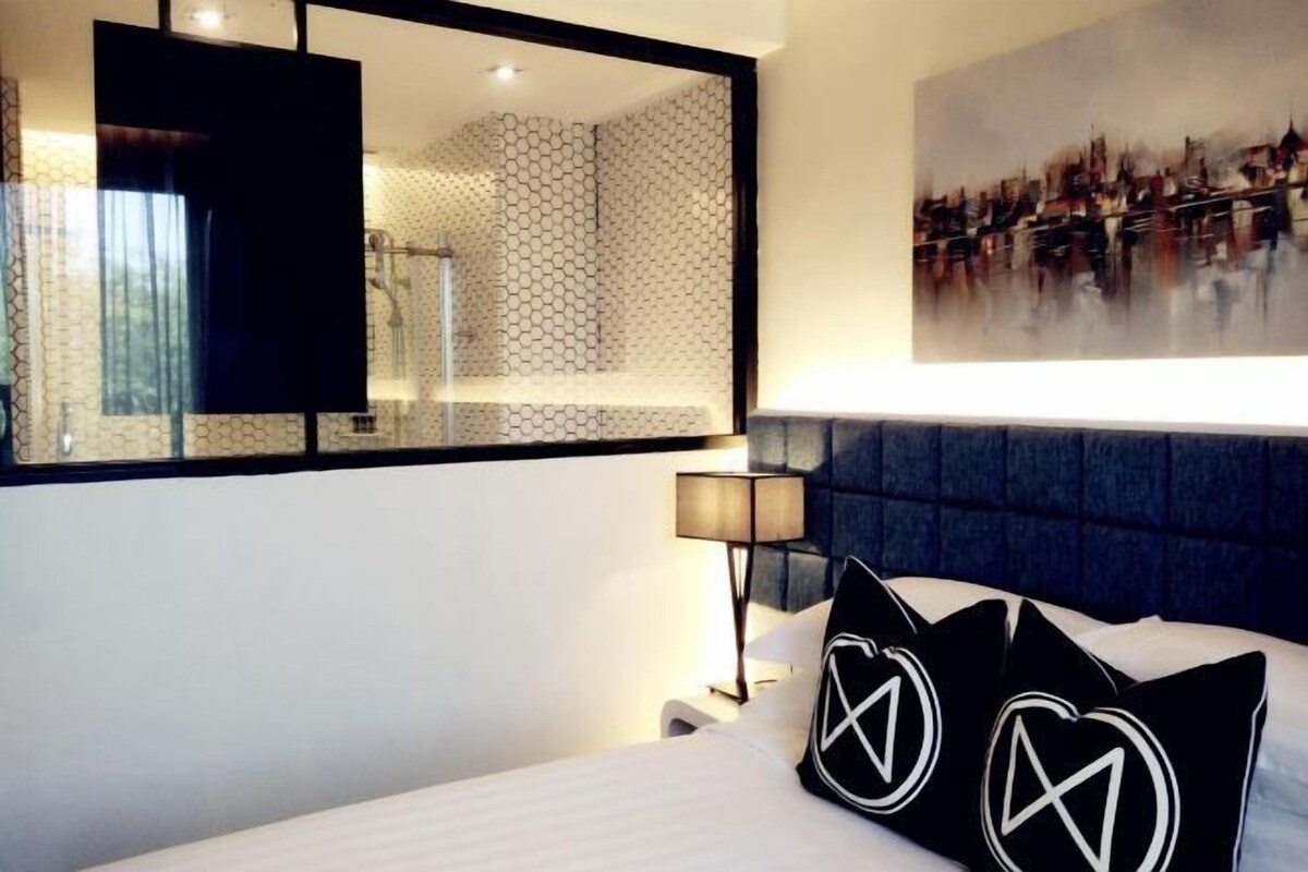 Ein modernes Hotelzimmer mit einem großen Bett, einem Kopfteil, einem Nachttisch, einer Lampe und einem Stadtbild an der Wand.