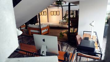 Un salón moderno con un sofá, un escritorio con una computadora y una mesa de centro. Hay cuadros enmarcados en la pared y una planta en una cesta.