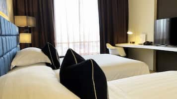 A hotel room with two beds, a desk, a TV, and a window with curtains.
