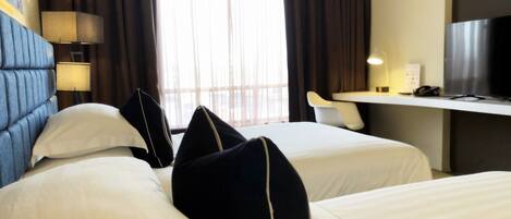 Habitación de hotel con dos camas, un escritorio, un televisor y una ventana con cortinas.