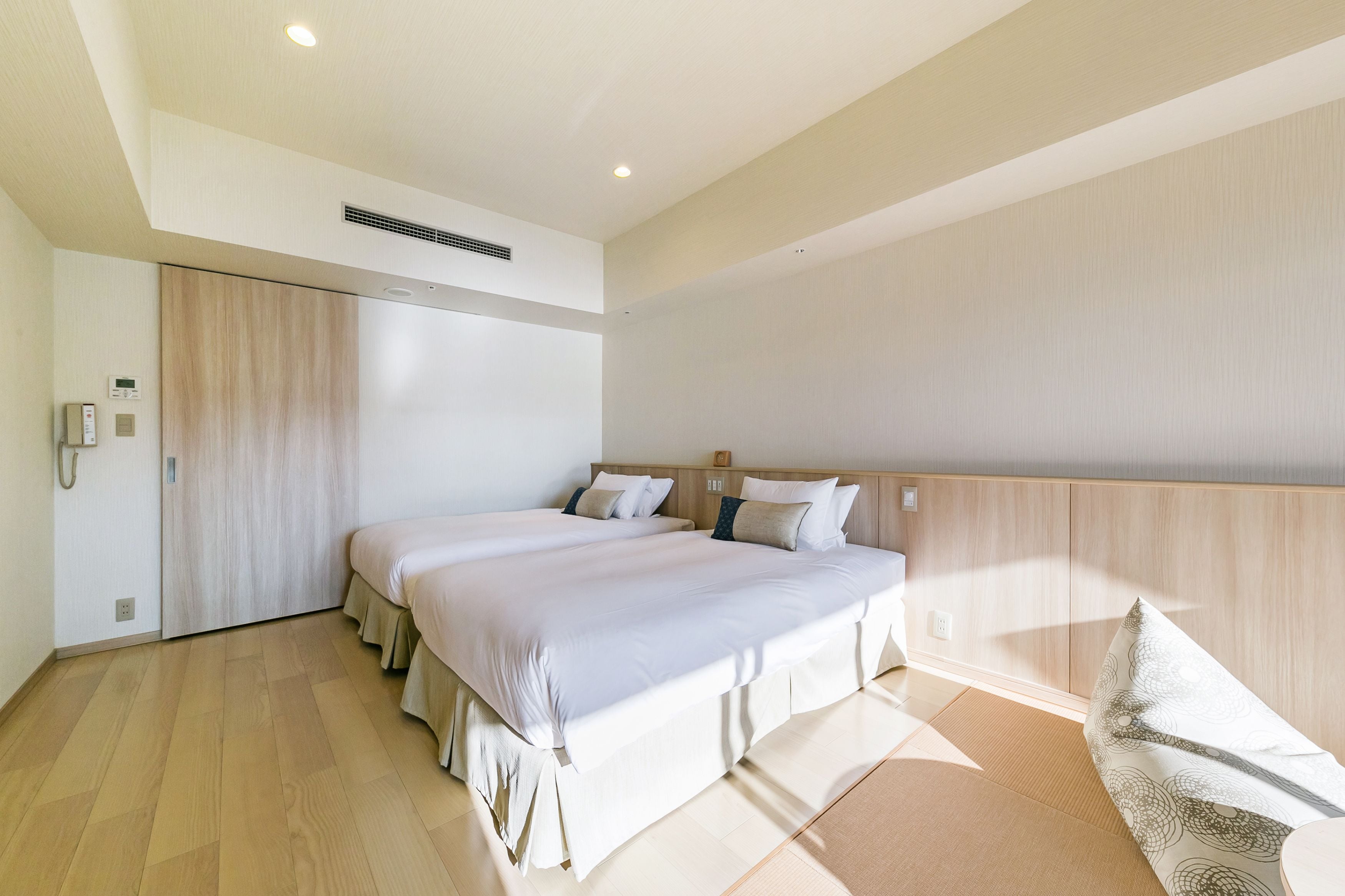 A modern bedroom with two beds, wooden flooring, and a large window.