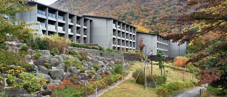 A modern building with multiple balconies, surrounded by a landscaped garden with rocks and shrubs, and a mountain in the background.